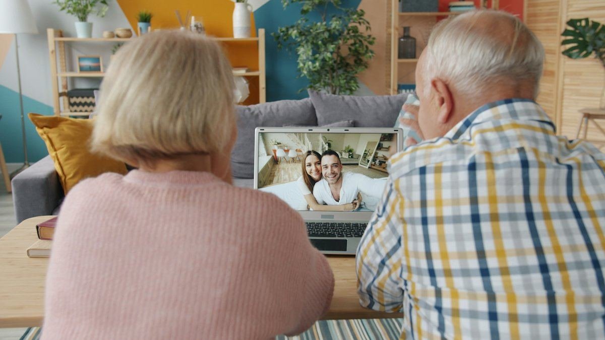 An older couple at home on a video call with a younger couple on a laptop