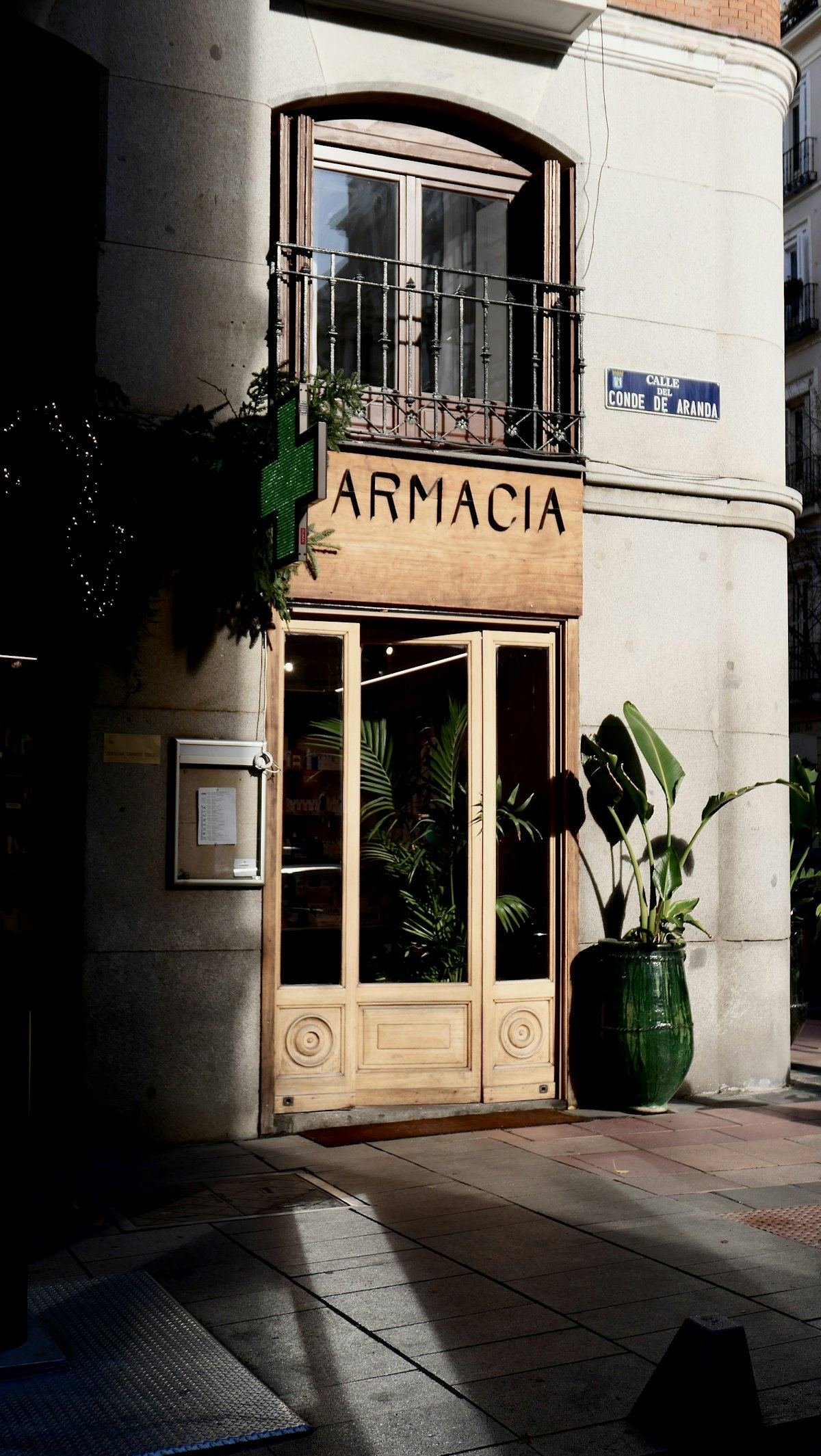 The entrance of a neighbourhood pharmacy with plants beside the door in the sunlight