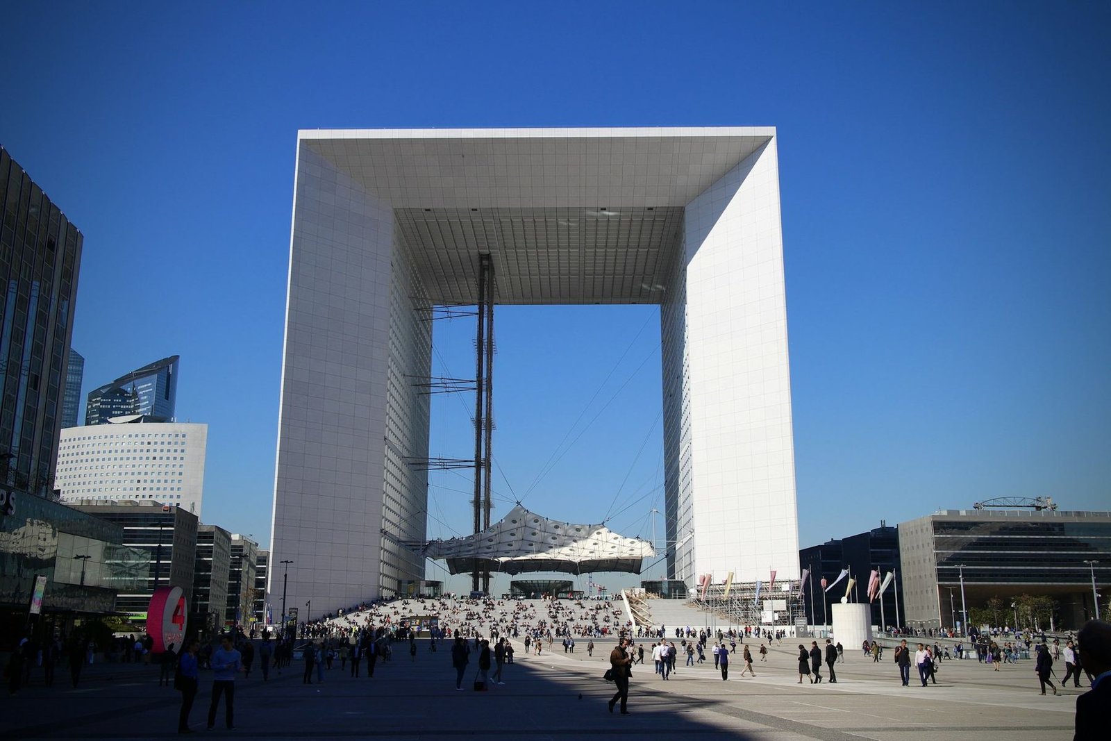 People crossing the wide plaza of La Défense in front of the Grande Arche