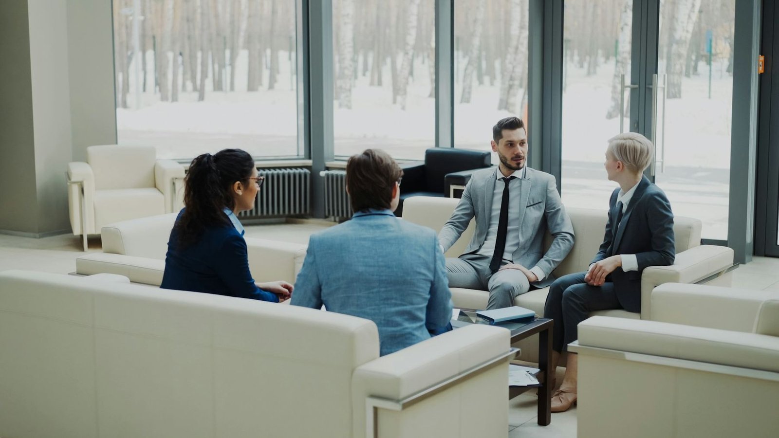 Four professionals in business dress talking in a bright office lounge
