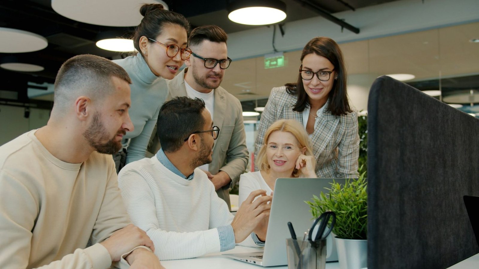 Colleagues of different backgrounds gathered around a laptop in an open-plan office